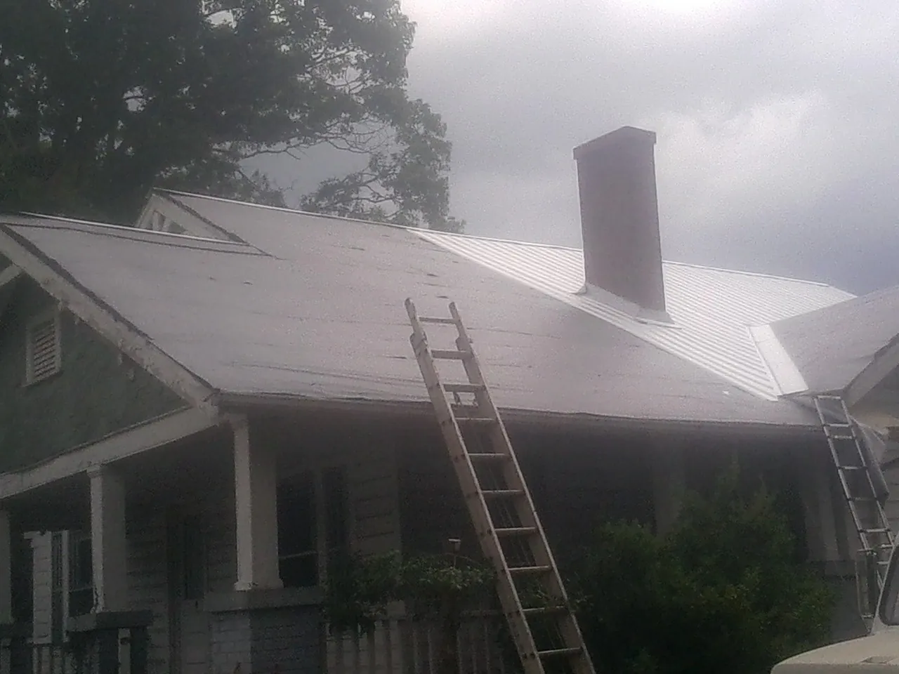 Ladders against a metal roof on an older home with a brick chimney in Annandale On Hudson
