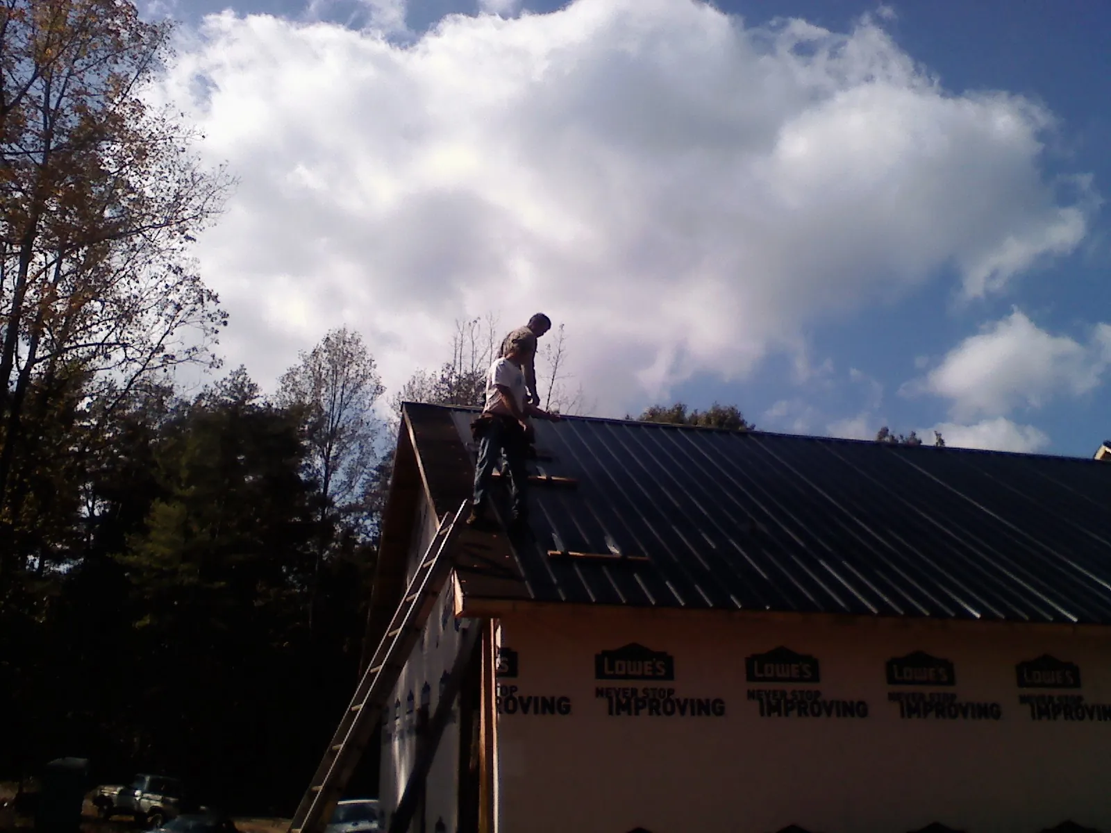 Roofer fastening dark metal panels high against a cloudy sky, from a Roof Inspection job in Annandale On Hudson