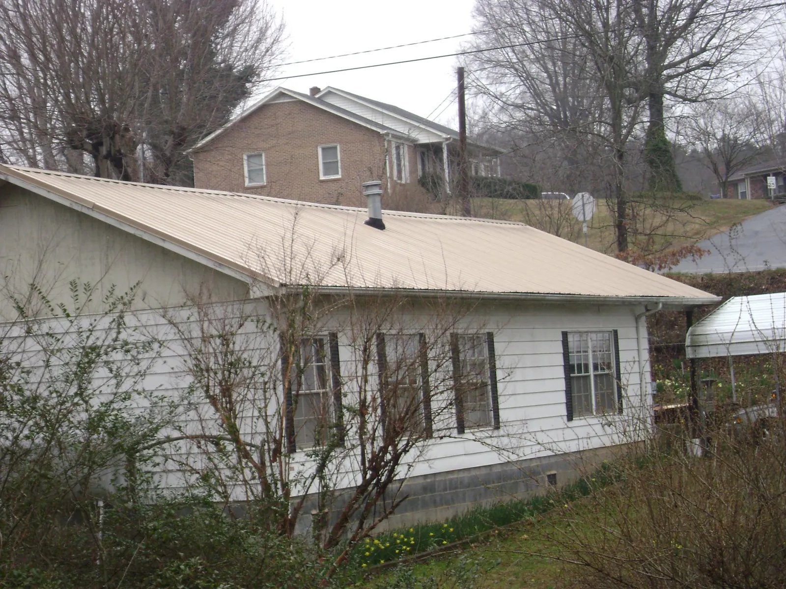 Tan metal roof on a white sided house set into a hillside — Commercial Roofing by Roofing Brothers in Annandale On Hudson